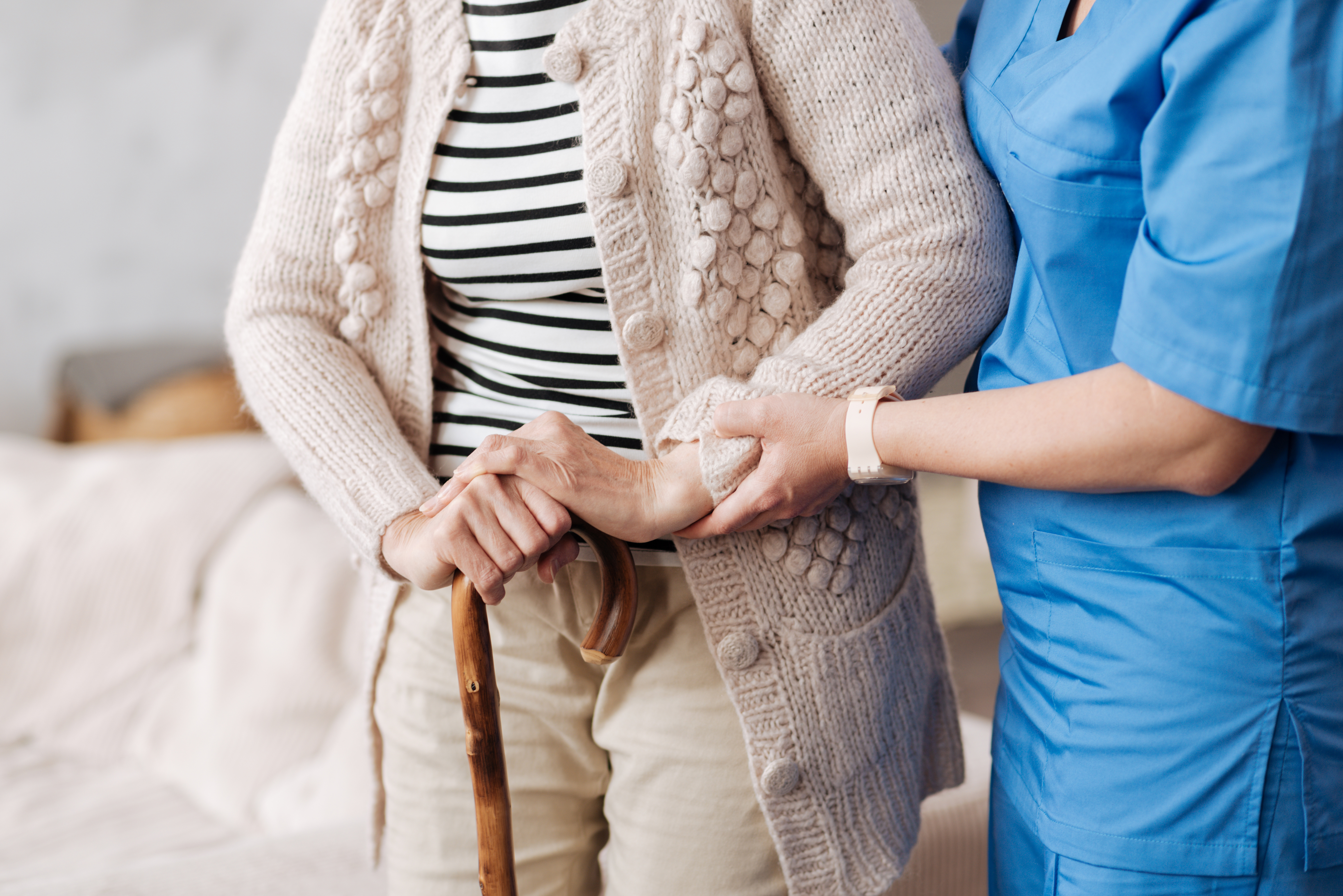 Pflegekraft stützt ältere Frau mit Gehstock
